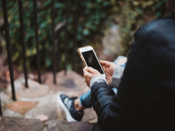 A woman using her phone while sitting on a step, to illustrate crossposting on social media